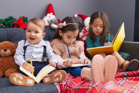 Téléchargez les photos : Groupe d'enfants dessin sur ordinateur portable assis sur le canapé par la décoration de Noël à la maison - en image libre de droit
