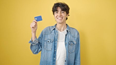 Photo for Young hispanic man smiling confident holding credit card over isolated yellow background - Royalty Free Image