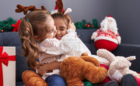 Photo for Two kids hugging teddy bear sitting on sofa by christmas decoration at home - Royalty Free Image