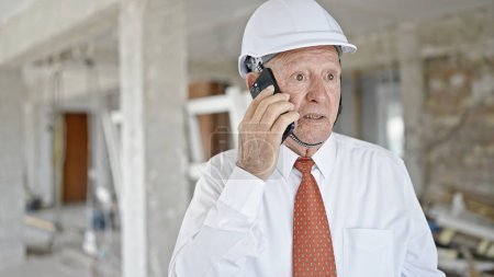 Photo for Senior grey-haired man architect talking on smartphone with relaxed expression at construction site - Royalty Free Image