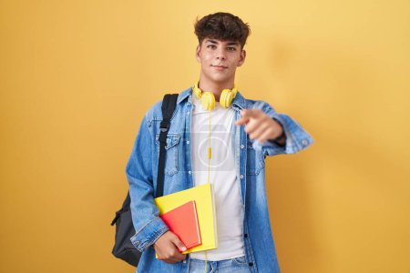 Photo for Hispanic teenager wearing student backpack and holding books pointing fingers to camera with happy and funny face. good energy and vibes. - Royalty Free Image