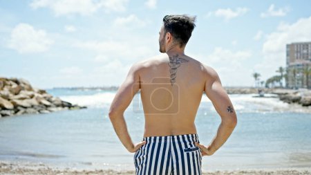 Photo for Young hispanic man tourist wearing swimsuit standing backwards at the beach - Royalty Free Image