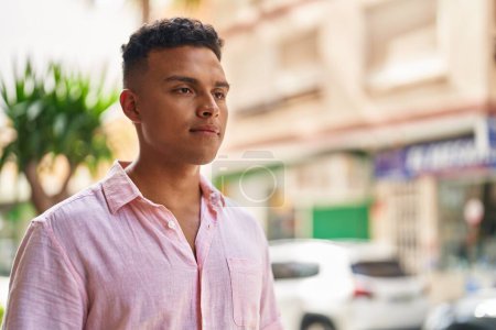 Téléchargez les photos : Jeune homme latino avec une expression détendue debout dans la rue - en image libre de droit