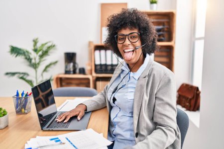 Photo for Black woman with curly hair wearing call center agent headset at the office sticking tongue out happy with funny expression. emotion concept. - Royalty Free Image
