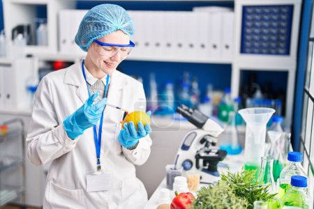 Téléchargez les photos : Jeune femme blonde scientifique injectant du citron au laboratoire - en image libre de droit
