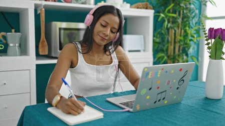 Téléchargez les photos : Femme afro-américaine écoutant de la musique écrire sur ordinateur portable à la salle à manger - en image libre de droit