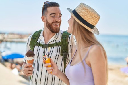 Foto de Hombre y mujer turista pareja sonriendo confiado comiendo helado en la playa - Imagen libre de derechos