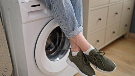 Photo for Young blonde woman sitting on washing machine at laundry room - Royalty Free Image