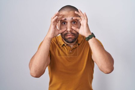 Téléchargez les photos : Hispanic man with beard standing over white background trying to open eyes with fingers, sleepy and tired for morning fatigue - en image libre de droit