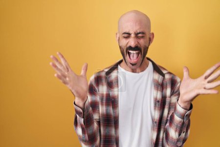 Téléchargez les photos : Hispanic man with beard standing over yellow background celebrating mad and crazy for success with arms raised and closed eyes screaming excited. winner concept - en image libre de droit