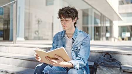 Téléchargez les photos : Jeune homme hispanique étudiant livre de lecture assis sur les escaliers à l'université - en image libre de droit