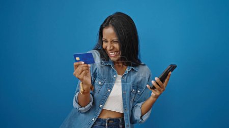 Photo for African american woman shopping with smartphone and credit card over isolated blue background - Royalty Free Image