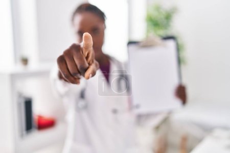 Photo for Beautiful black doctor woman holding clipboard pointing with finger to the camera and to you, confident gesture looking serious - Royalty Free Image