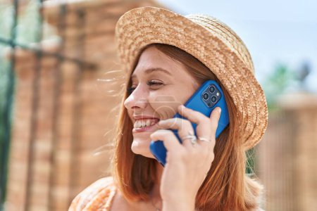 Foto de Mujer pelirroja joven turista con sombrero de verano hablando en el teléfono inteligente en la calle - Imagen libre de derechos