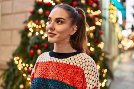 Téléchargez les photos : Jeune femme souriante confiante debout près de l'arbre de Noël dans la rue - en image libre de droit