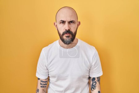 Photo for Young hispanic man with tattoos standing over yellow background looking sleepy and tired, exhausted for fatigue and hangover, lazy eyes in the morning. - Royalty Free Image