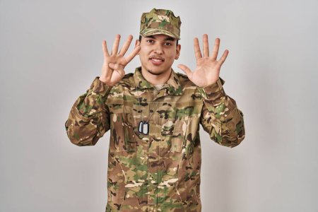 Foto de Joven árabe vestido con camuflaje uniforme del ejército mostrando y señalando hacia arriba con los dedos número nueve mientras sonríe confiado y feliz. - Imagen libre de derechos