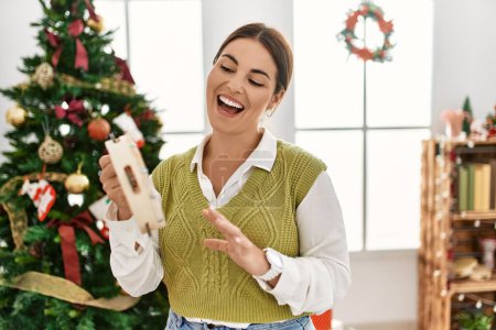 Téléchargez les photos : Jeune belle femme hispanique jouant au tambourin debout près de l'arbre de Noël à la maison - en image libre de droit