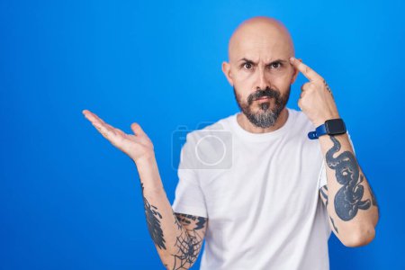 Photo for Hispanic man with tattoos standing over blue background confused and annoyed with open palm showing copy space and pointing finger to forehead. think about it. - Royalty Free Image