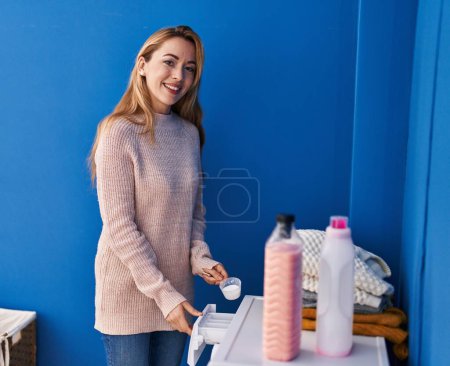 Téléchargez les photos : Jeune femme souriante confiante détergent versant sur la machine à laver à la buanderie - en image libre de droit