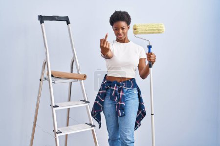 Téléchargez les photos : African american woman holding roller painter showing middle finger, impolite and rude fuck off expression - en image libre de droit