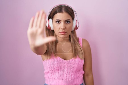 Photo for Young blonde woman listening to music using headphones doing stop sing with palm of the hand. warning expression with negative and serious gesture on the face. - Royalty Free Image