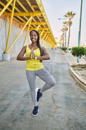 Téléchargez les photos : Femme afro-américaine portant des vêtements de sport faisant de l'exercice de yoga dans la rue - en image libre de droit
