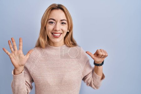 Foto de Mujer hispana de pie sobre fondo azul mostrando y señalando hacia arriba con los dedos número seis mientras sonríe confiada y feliz. - Imagen libre de derechos