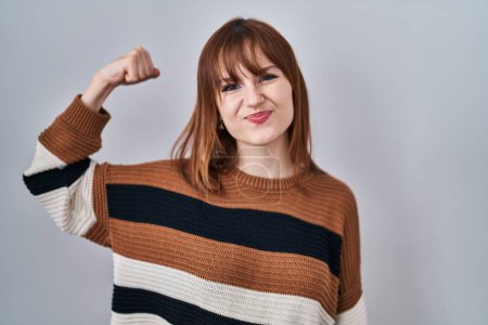 Photo for Young beautiful woman wearing striped sweater over isolated background strong person showing arm muscle, confident and proud of power - Royalty Free Image
