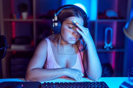 Photo for Young blonde woman playing video games wearing headphones tired rubbing nose and eyes feeling fatigue and headache. stress and frustration concept. - Royalty Free Image