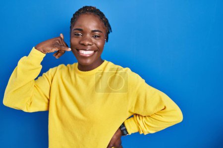 Téléchargez les photos : Belle femme noire debout sur fond bleu souriant faisant geste de téléphone avec la main et les doigts comme parler au téléphone. communiquer les concepts. - en image libre de droit