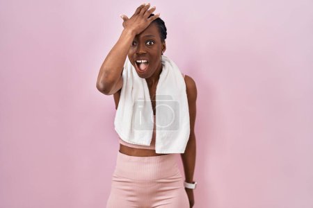 Téléchargez les photos : Belle femme noire portant des vêtements de sport et une serviette sur fond rose surpris avec la main sur la tête pour erreur, rappelez-vous erreur. oublié, mauvais concept de mémoire. - en image libre de droit