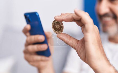 Foto de Hombre de mediana edad con criptomoneda de cardano usando teléfono inteligente en casa - Imagen libre de derechos