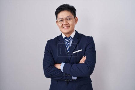 Téléchargez les photos : Jeune homme asiatique portant un costume d'affaires et cravate visage heureux souriant avec les bras croisés regardant la caméra. personne positive. - en image libre de droit