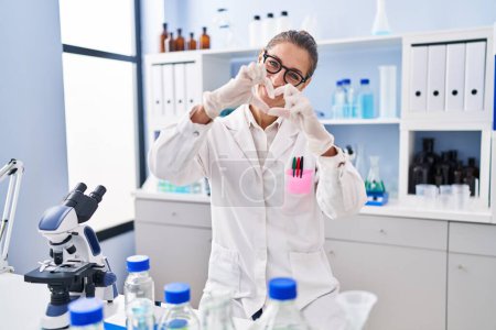Photo for Young woman working at scientist laboratory smiling in love doing heart symbol shape with hands. romantic concept. - Royalty Free Image