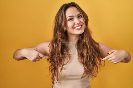 Photo for Young hispanic woman standing over yellow background looking confident with smile on face, pointing oneself with fingers proud and happy. - Royalty Free Image