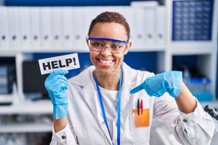 Foto de Hermosa mujer afroamericana que trabaja en el laboratorio científico pidiendo ayuda señalando con el dedo a uno mismo sonriendo feliz y orgulloso - Imagen libre de derechos