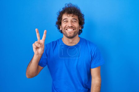 Téléchargez les photos : Hispanic young man standing over blue background showing and pointing up with fingers number two while smiling confident and happy. - en image libre de droit