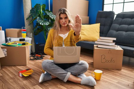 Photo for Young woman sitting on the floor at new home using laptop doing stop sing with palm of the hand. warning expression with negative and serious gesture on the face. - Royalty Free Image