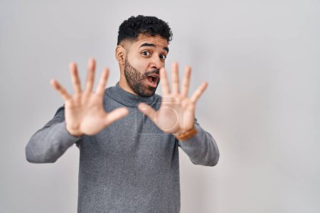 Foto de Hispanic man with beard standing over white background afraid and terrified with fear expression stop gesture with hands, shouting in shock. panic concept. - Imagen libre de derechos