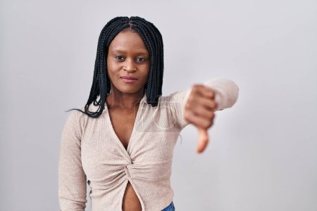 Téléchargez les photos : Femme africaine avec des tresses debout sur fond blanc regardant malheureux et en colère montrant rejet et négatif avec les pouces vers le bas geste. mauvaise expression. - en image libre de droit