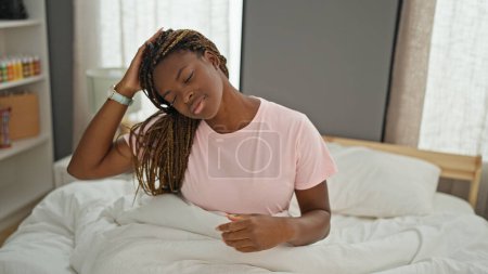 Téléchargez les photos : Femme afro-américaine assise sur le lit étirant la tête à la chambre - en image libre de droit