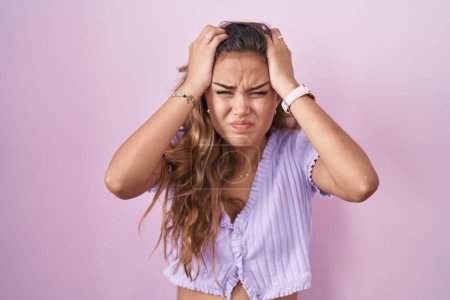 Photo for Young hispanic woman standing over pink background suffering from headache desperate and stressed because pain and migraine. hands on head. - Royalty Free Image