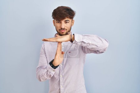 Téléchargez les photos : Homme arabe avec la barbe debout sur fond bleu faire le temps geste avec les mains, visage frustré et sérieux - en image libre de droit