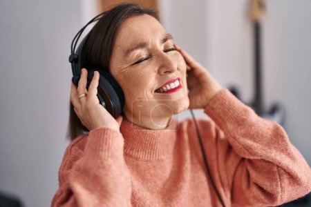 Foto de Middle age woman musician listening to music at music studio - Imagen libre de derechos