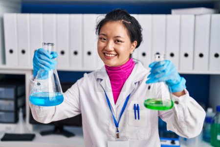 Foto de Joven científica china sonriendo confiada sosteniendo tubos de ensayo en el laboratorio - Imagen libre de derechos