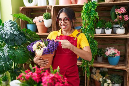 Téléchargez les photos : Jeune femme arabe travaillant au magasin de fleuriste tenant usine souriant heureux pointant avec la main et le doigt - en image libre de droit