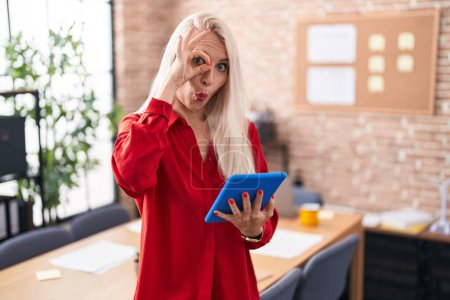 Téléchargez les photos : Femme caucasienne travaillant au bureau avec une tablette faisant un geste correct choqué par le visage surpris, les yeux regardant à travers les doigts. expression incrédule. - en image libre de droit