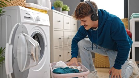 Téléchargez les photos : Jeune homme hispanique écoutant de la musique laver les vêtements à la buanderie - en image libre de droit