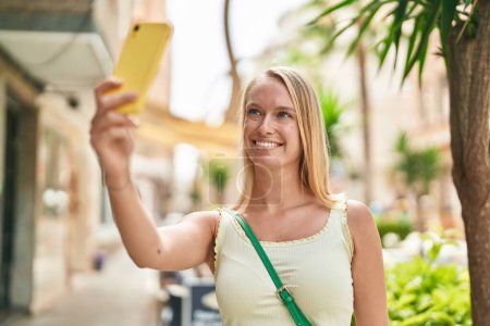 Foto de Young blonde woman smiling confident making selfie by the smartphone at street - Imagen libre de derechos